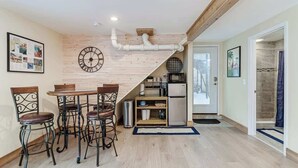 A compact kitchen with a wooden wall, a clock, and a dining area with metal chairs. - Studio Apartment w/ King Bed & Kitchenette (Lakeland)