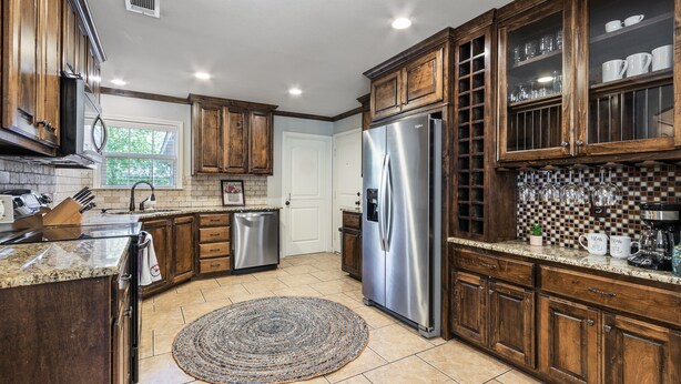 A kitchen with wooden cabinets, stainless steel appliances, and a tiled backsplash. - La Casa Roja - Pet-Friendly - 3BR Home - Walk to Castle & Downtown Waco (Waco)
