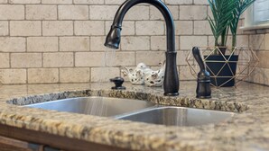 A kitchen with a granite countertop, a double sink, and a black faucet. - La Casa Roja - Pet-Friendly - 3BR Home - Walk to Castle & Downtown Waco (Waco)