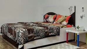 Une chambre à coucher avec un lit, un ventilateur de plafond, une étagère en bois, une table de chevet avec un téléphone et une petite plante.