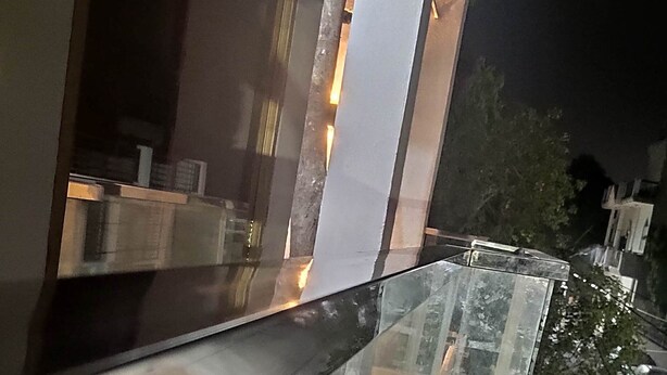 Une vue nocturne d’une rue bordée de voitures garées et d’un immeuble à l’architecture moderne.