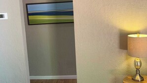 Une pièce avec un plancher en bois, une lampe sur une table d’appoint et un tableau au mur.