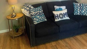 Un salon avec un canapé noir, deux tableaux abstraits bleus, une lampe et des coussins à motifs.
