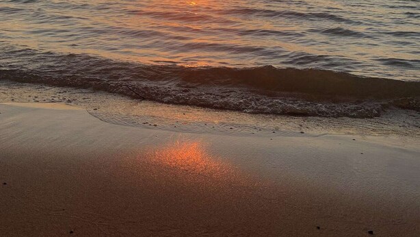 Une plage au coucher du soleil, avec le soleil qui disparaît à l’horizon.