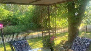 Une table à plateau en verre, entourée de chaises, se trouve sur une terrasse en bois, sous une pergola.