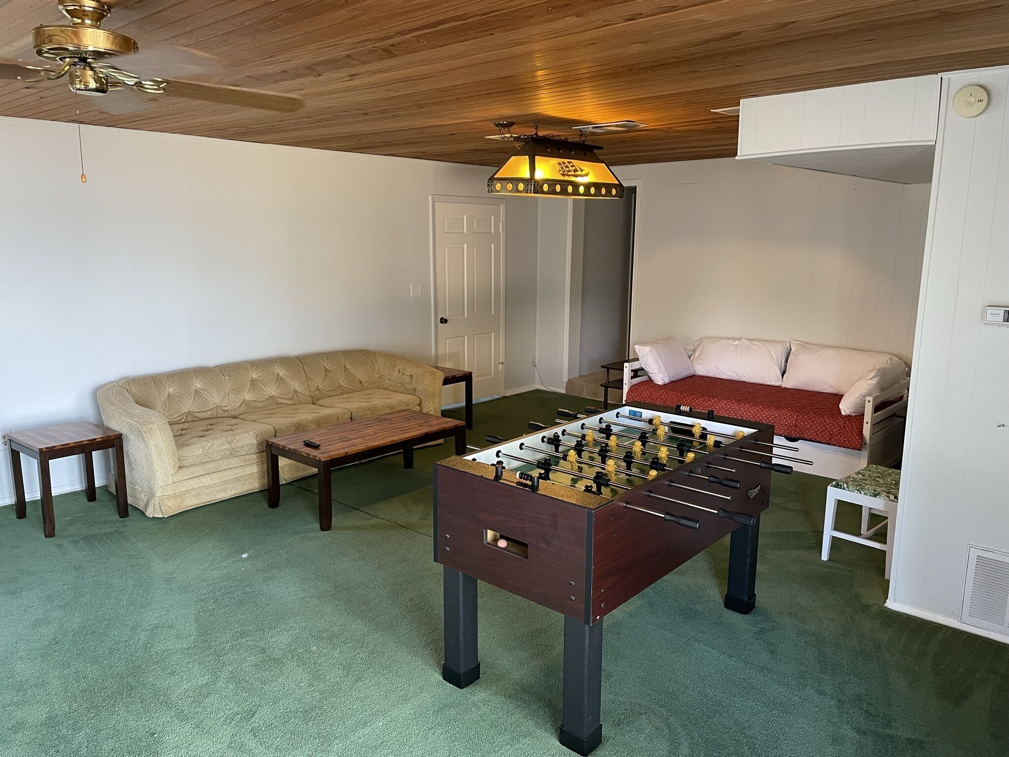 A living room with a sofa, a coffee table, a foosball table, a ceiling fan, and a door.
