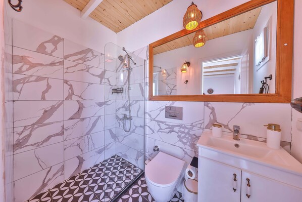 A bathroom with a glass shower enclosure, a toilet, a sink with a mirror, and patterned tiles.