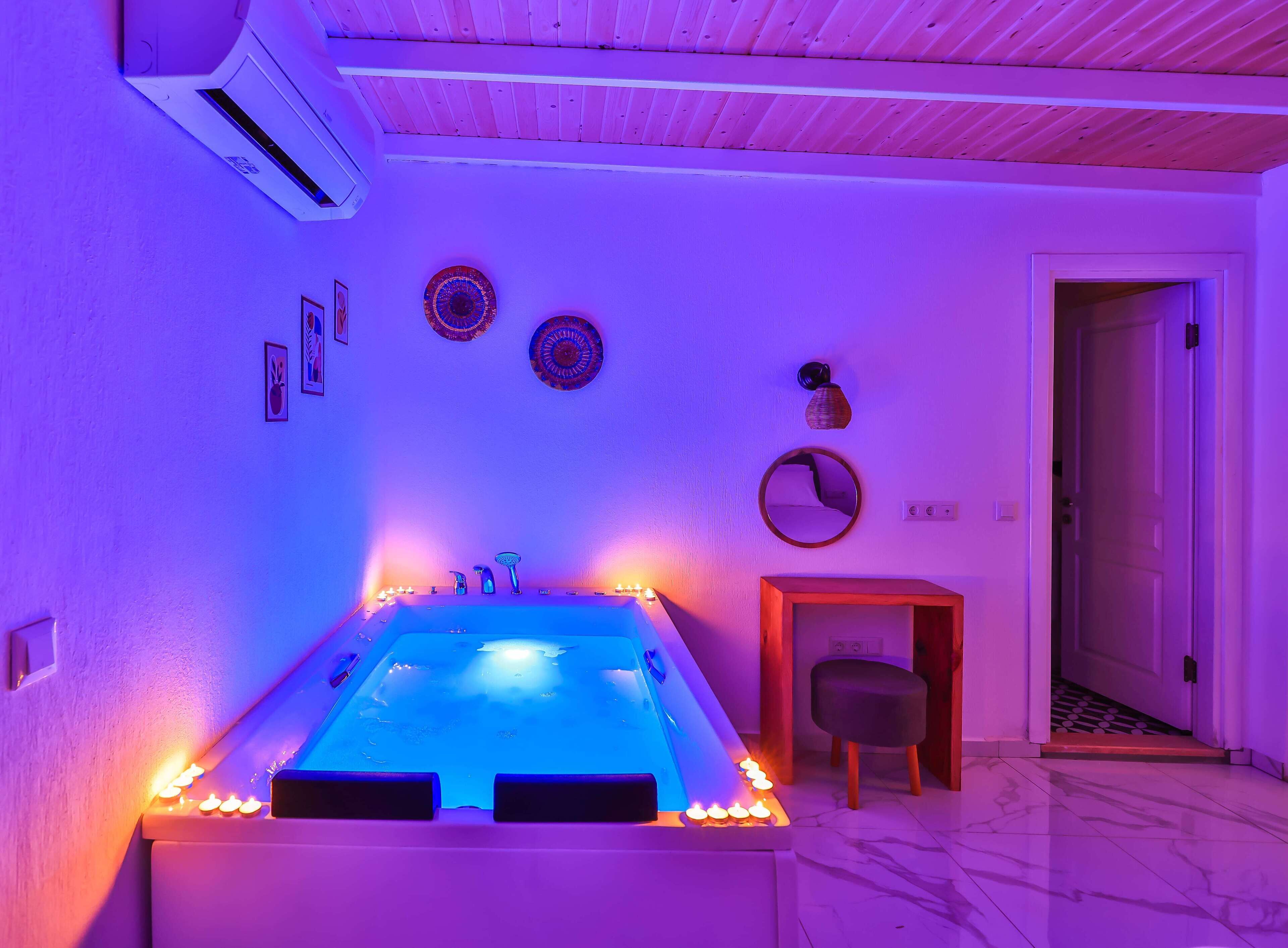 A room with a bathtub, wall-mounted air conditioning, decorative plates, a mirror, and a small wooden cabinet.