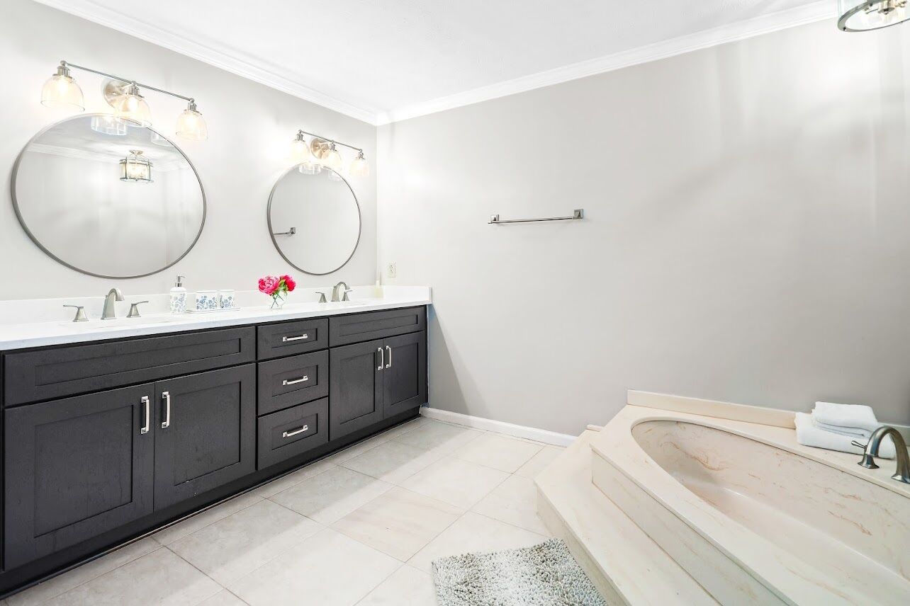 A modern bathroom with a double vanity, large mirrors, and a freestanding bathtub.