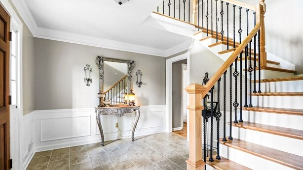 Un magnifique escalier en bois, avec des marches en bois et des balustrades noires, menant à un palier agrémenté d’un miroir décoratif et d’appliques murales.