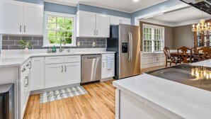 Une cuisine moderne avec des meubles blancs, un réfrigérateur en acier inoxydable et un plancher en bois.