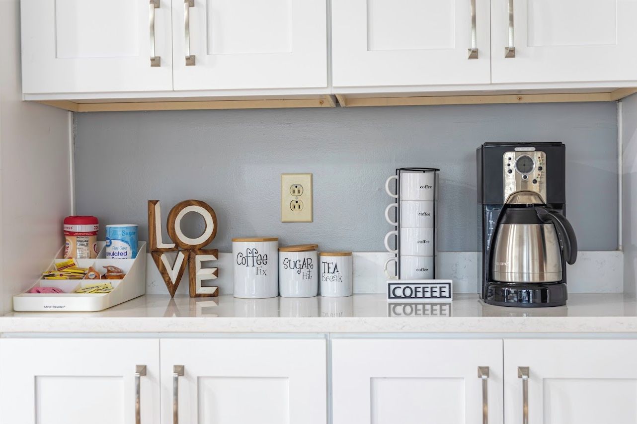 A kitchen counter with white cabinets, a coffee maker, and labeled containers for coffee, sugar, and tea.