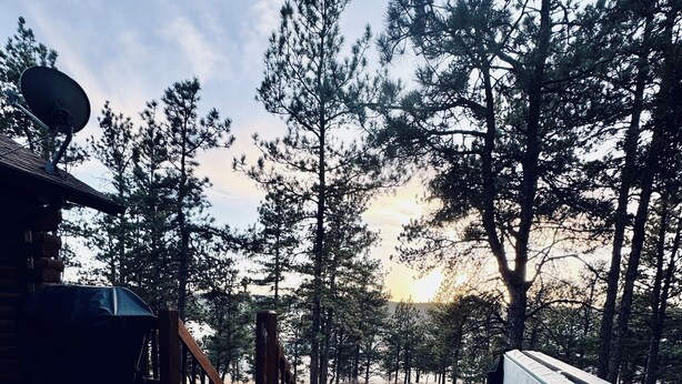 Ett bubbelbad i ett skogsområde med ett trädäck och en byggnad i bakgrunden.