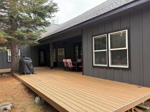 A covered deck area with a grill, outdoor seating, and a large window.