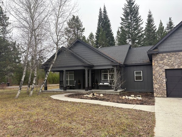 A two-story house with a stone facade, a covered porch with seating, and a well-maintained lawn.