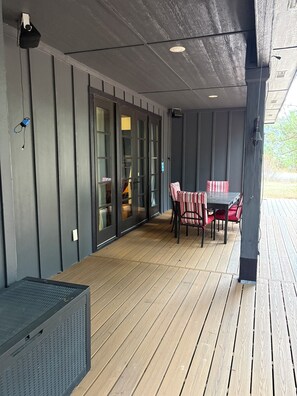 Un patio couvert doté d’une terrasse en bois, d’une table avec des chaises et d’une porte-fenêtre coulissante donnant sur un espace intérieur.