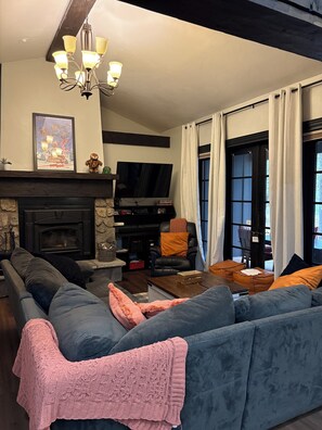A living room with a fireplace, a large sofa, a television, and a window with curtains.