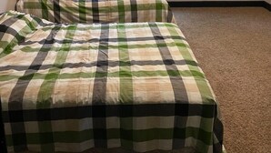 Une chambre avec un lit simple, des murs de couleur beige, une fenêtre donnant sur des arbres et un sol recouvert de moquette.