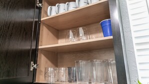 Eine Küchenschrank mit mehreren Einlegeböden, auf denen diverses Glas und ein blauer Behälter stehen.