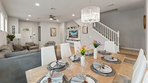 Un comedor con una mesa de madera dispuesta para cuatro comensales, sillas blancas y un candelabro.