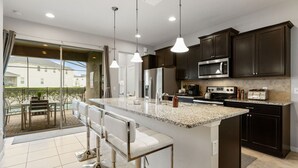 Una cocina moderna con armarios oscuros, encimera de granito, electrodomésticos de acero inoxidable y una zona de bar con taburetes.