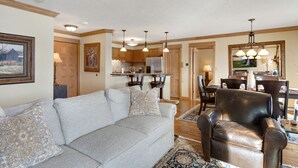Ein Wohnzimmer mit grauem Sofa, Ledersessel und Essbereich mit Holzsäulen und Pendelleuchten.
