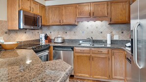 Eine moderne Küche mit Holzschränken, Edelstahlgeräten, Granitarbeitsplatten und einer gemusterten Spritzschutzwand.