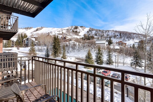 A balcony with a view of a snowy mountain landscape, a pool, and a parking area with cars.