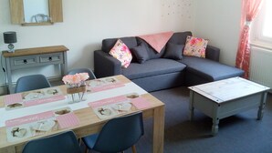 Una sala de estar acogedora con un sofá, una mesa de comedor y una mesa de centro. Hay un espejo en la pared y un adorno sobre el sofá.