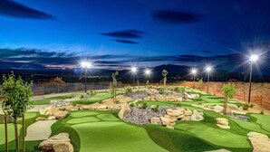 A golf course at night with illuminated lights, green fairways, and rocky terrain.