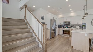 A modern kitchen with wooden flooring, white cabinets, stainless steel appliances, and pendant lighting.
