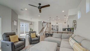 A spacious living room with a sectional sofa, a recliner, and a coffee table. A staircase leads to a kitchen area with bar stools.