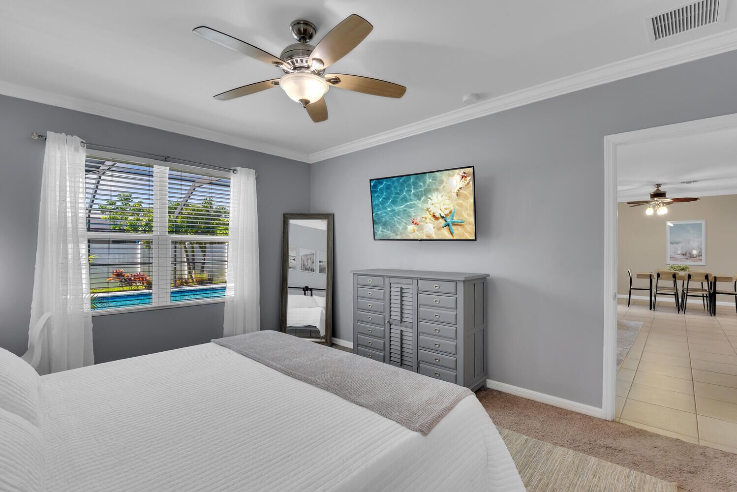 A bedroom with a bed, a ceiling fan, a window with blinds, a dresser, and a painting on the wall.