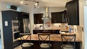 Una cocina moderna con armarios oscuros, electrodomésticos de acero inoxidable y una isla central con taburetes de bar.