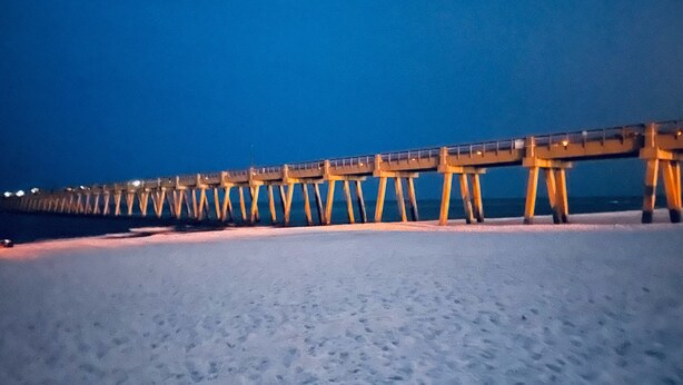 Un muelle se adentra en el agua de noche, con una playa arenosa al frente.