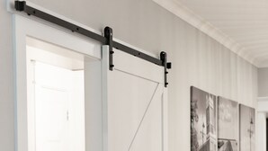 Un couloir avec une porte de grange coulissante blanche, un plancher en bois et des photographies en noir et blanc accrochées au mur.