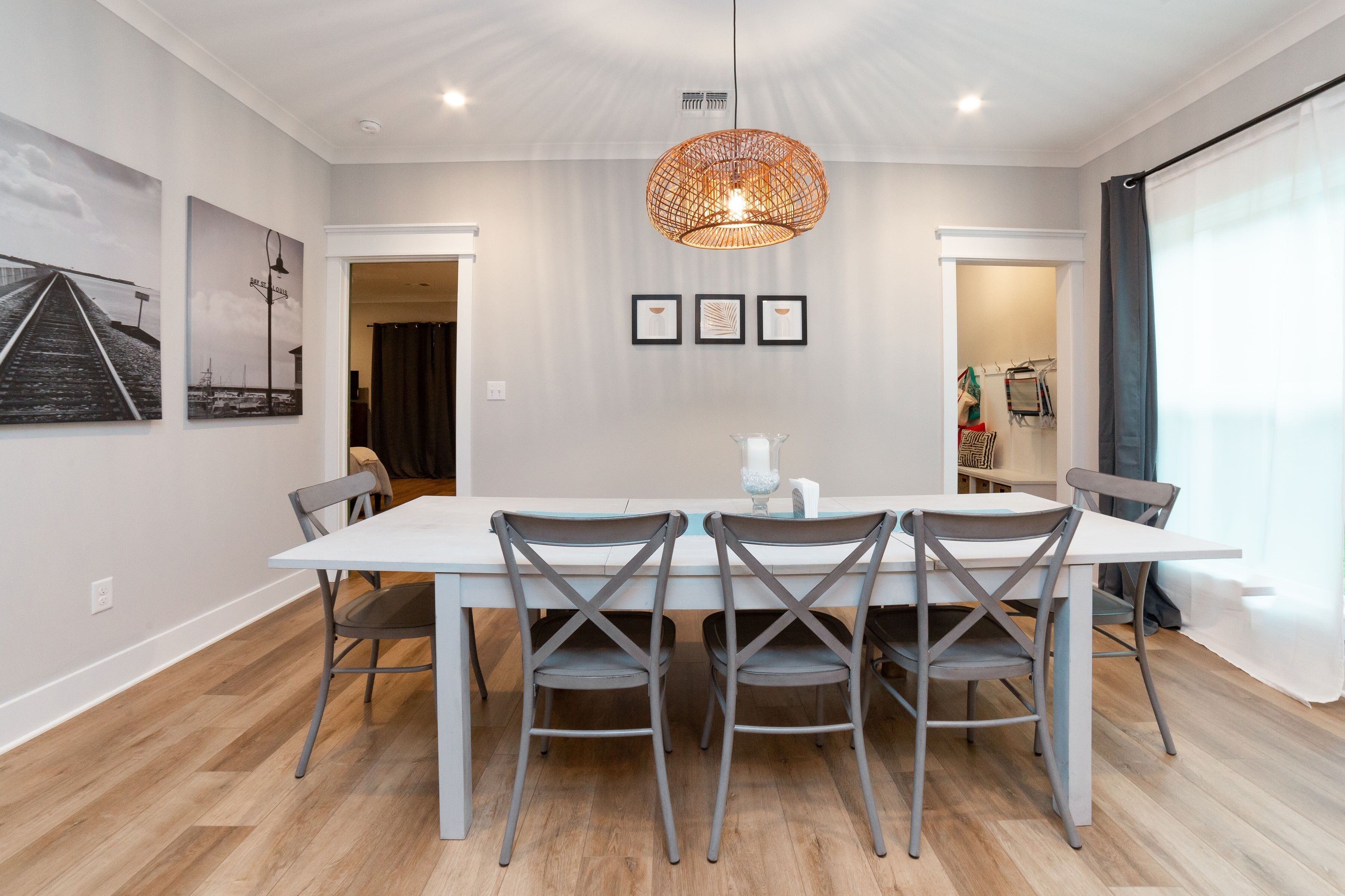 Un coin repas avec une table blanche et des chaises grises, un luminaire suspendu et des tableaux encadrés au mur.