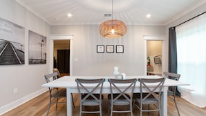 Un coin repas avec une table blanche et des chaises grises, un luminaire suspendu et des tableaux encadrés au mur.