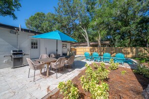 A backyard with a barbecue grill, a table with chairs, a blue umbrella, and a wooden fence. - Cozy Retreat w/ Heated Pool & Yard Near Downtown (Tampa)