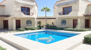 A swimming pool with a turtle, surrounded by two-story buildings with balconies and a palm tree. - Villa Sonari 2 by Kivoya (Puerto Peñasco)