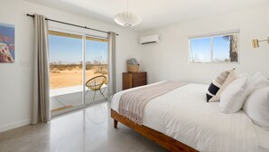 A bedroom with a large bed, a chair, a dresser, and a window with a view of the desert.