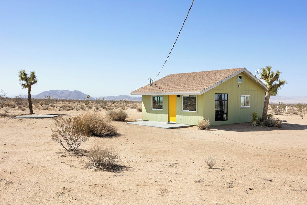 A single-story house with a flat roof, a yellow door, and a small front porch.