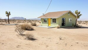A single-story house with a flat roof, a yellow door, and a small front porch. - Green Jackrabbit - Hot Tub + Endless Desert Views! (Joshua Tree)