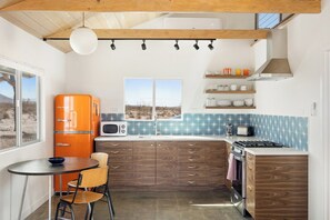 A compact kitchen with a wooden ceiling, a built-in microwave, a stove, and a window with a view.