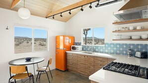 A kitchen with a modern design, featuring a large window, an orange refrigerator, and a gas stove.