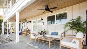 A covered outdoor seating area with wooden furniture, a ceiling fan, and potted plants. - Hale 'Io • Remodeled 2/2 Luxury • AC • Ocean View (Kailua-Kona)