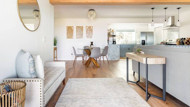 A modern kitchen with a central island, a dining area with a round table and chairs, and a living area with a sofa and a large mirror. - Hale 'Io • Remodeled 2/2 Luxury • AC • Ocean View (Kailua-Kona)