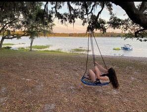 Eine Person schwingt in einem Park, im Hintergrund ein See und Boote.