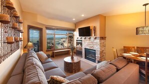 A spacious living room with a large sofa, a fireplace, a television, and a view of the city. - Rooftop Hot Tub + Outdoor Pool | Ski-in/Ski-out (Park City)