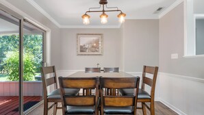 A dining area with a large table, four chairs, a chandelier, and a framed picture on the wall.